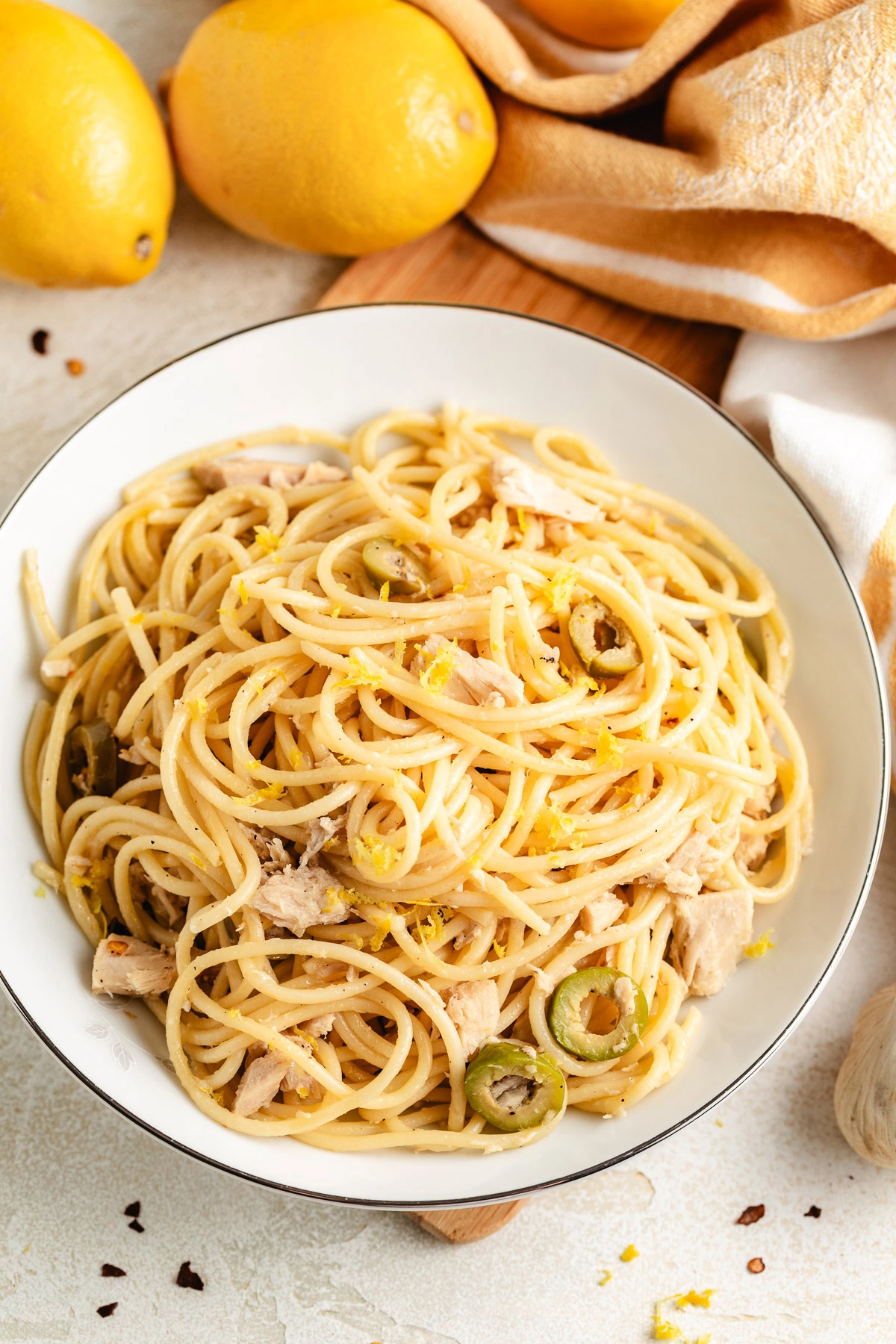 Plate of lemon garlic spaghetti with tuna and olives near whole lemons.