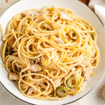 Bowl of canned tuna pasta with lemon zest and sliced green olives.