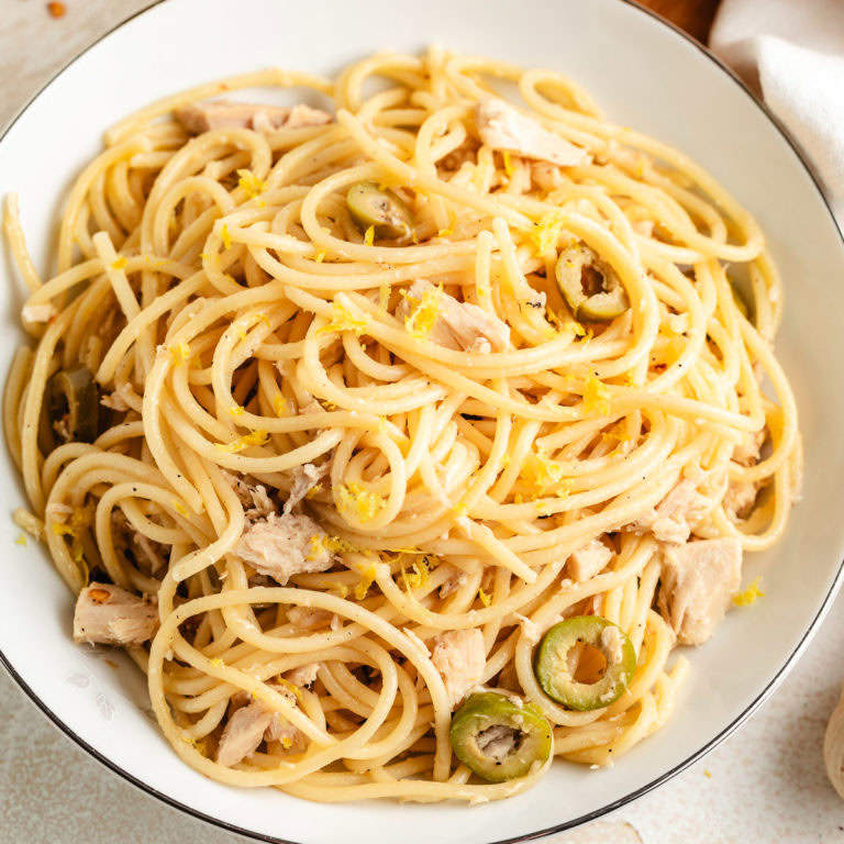 Bowl of canned tuna pasta with lemon zest and sliced green olives.