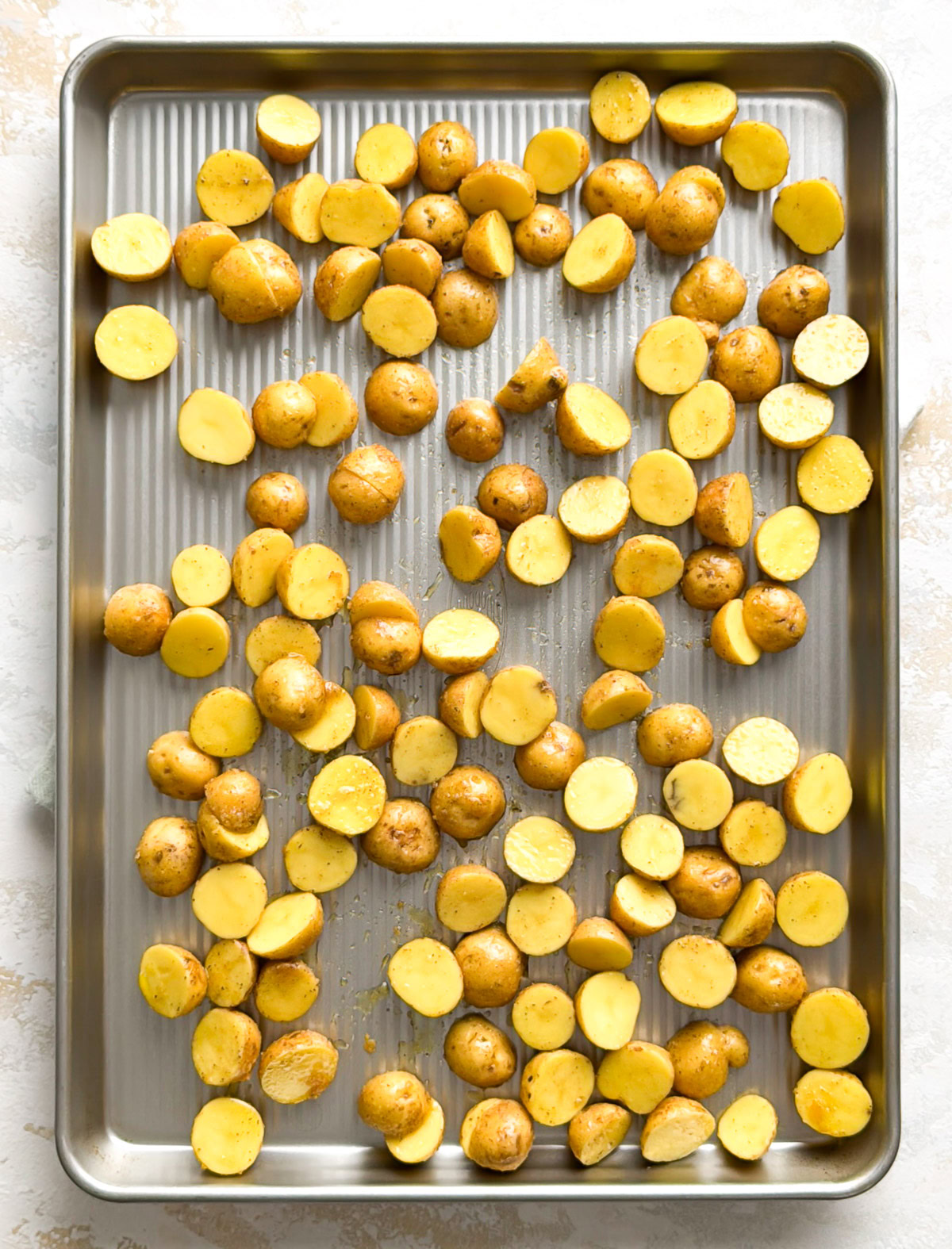 Seasoned potatoes spread out on a sheet pan.