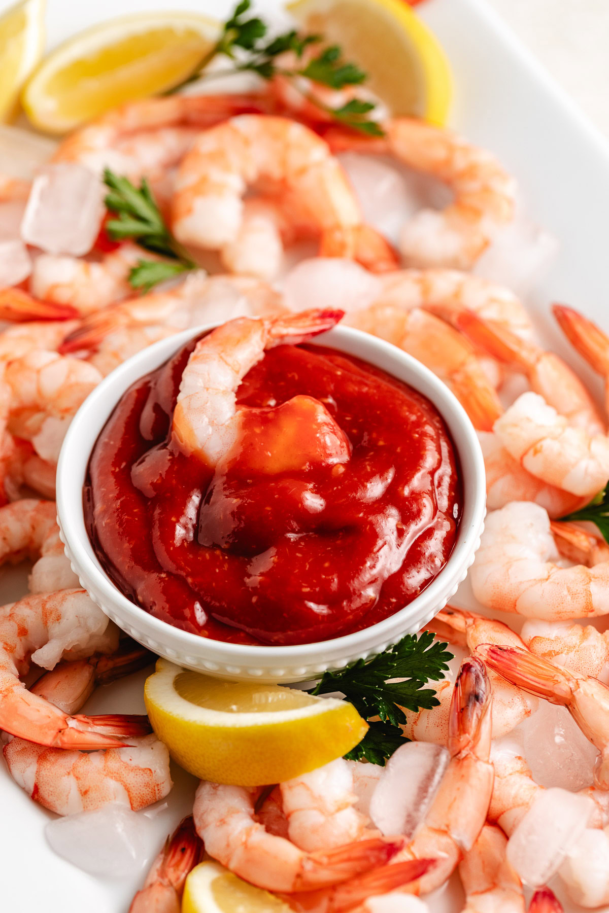 Bowl of shrimp cocktail sauce with chilled shrimp and lemon wedges on a platter.