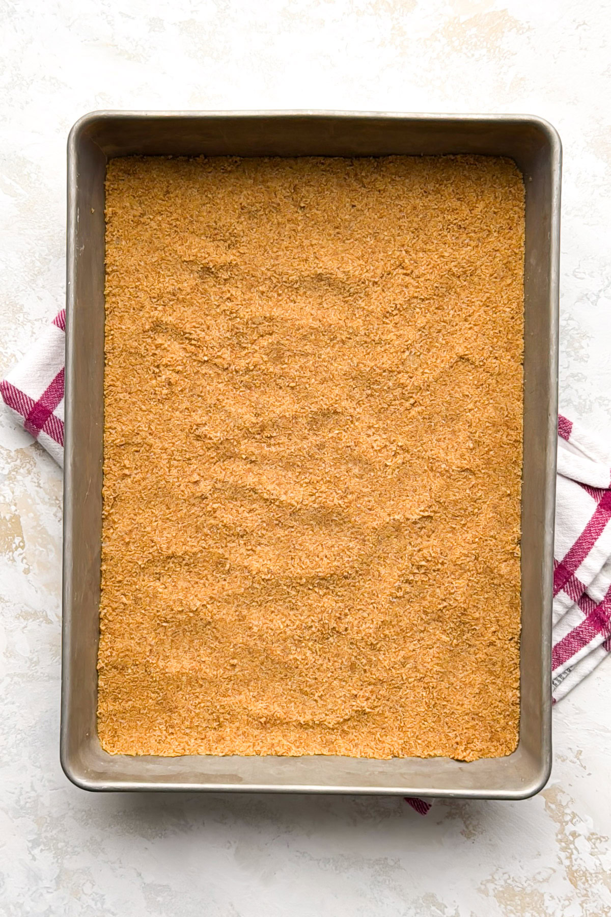 Baked graham cracker crust in a metal baking pan.