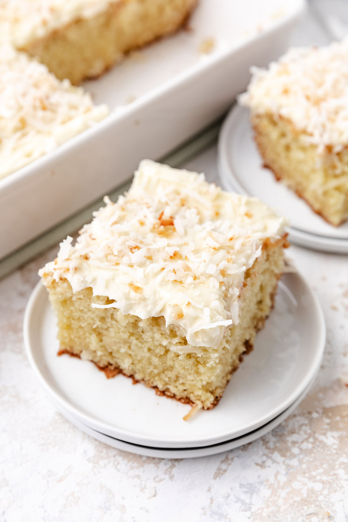 A tall slice of coconut cake on a white plate.