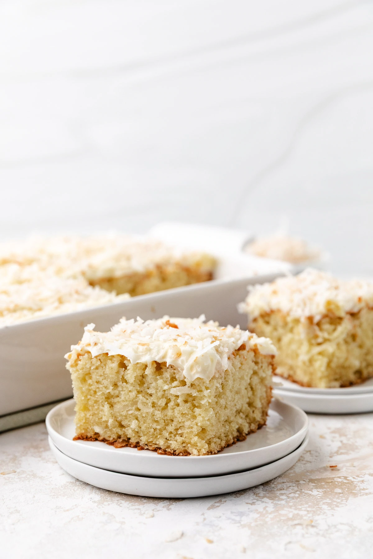 A frosted slice of coconut cake on a white plate.