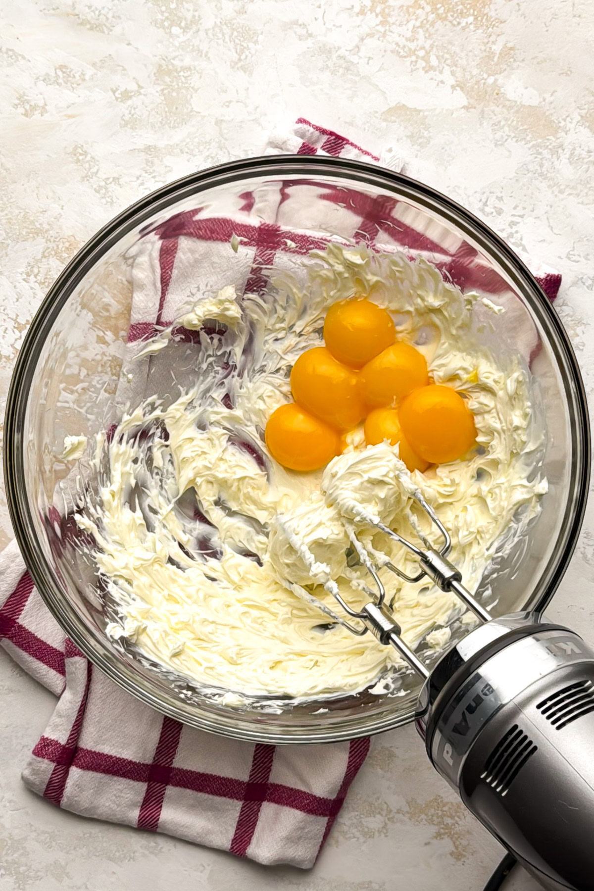 Softened cream cheese and egg yolks in a glass mixing bowl.