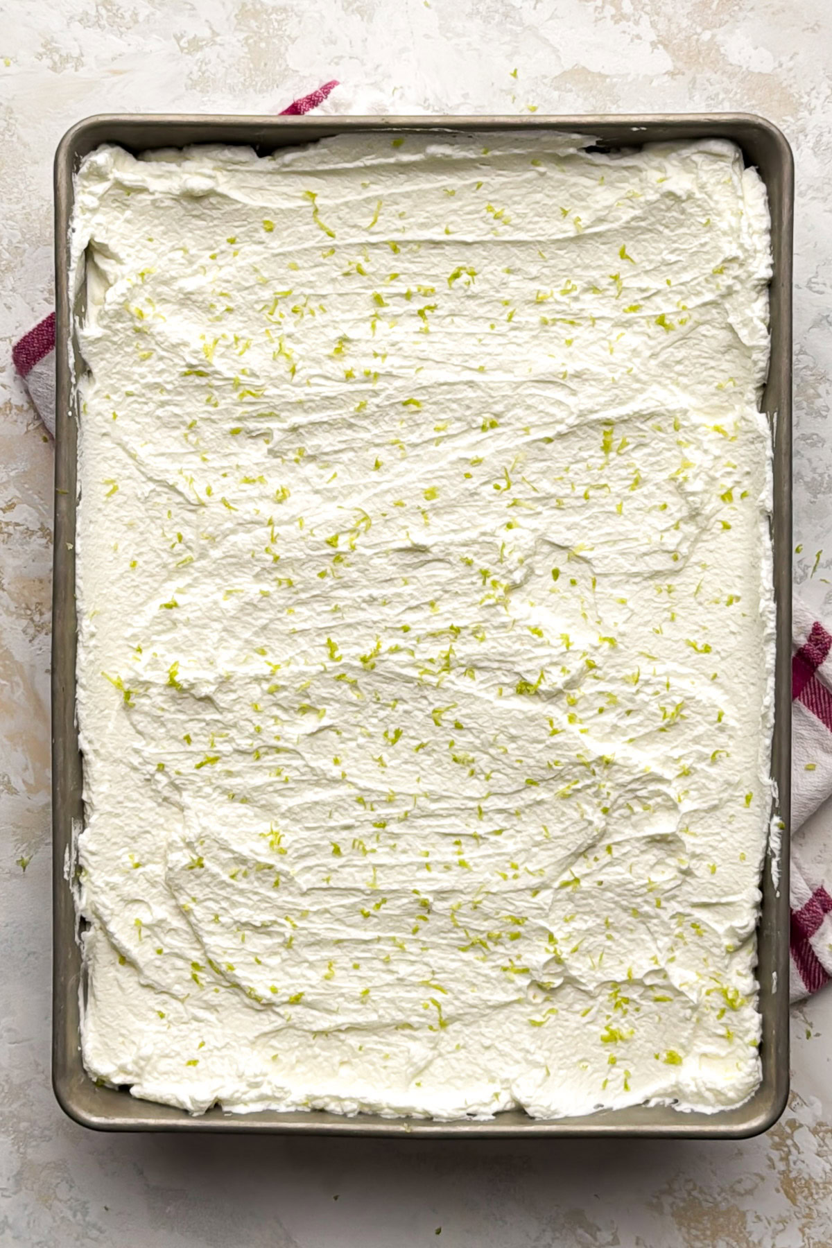 Key lime bars topped with whipped cream and lime zest in the baking pan.