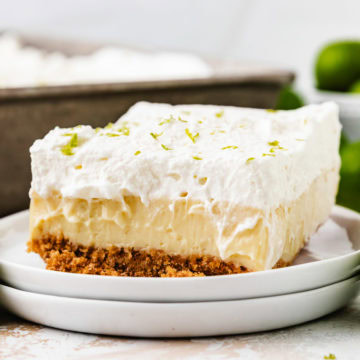 A thick slice of key lime pie bars topped with whipped cream and lime zest.
