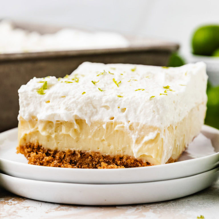 A thick slice of key lime pie bars topped with whipped cream and lime zest.